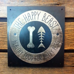 Metal sign logo for The Happy Beast, a natural pet store in Lafayette, CO